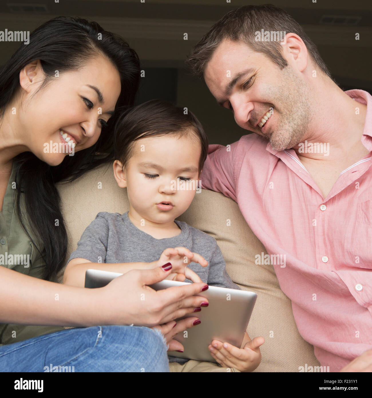 Eltern sitzen auf einem Sofa mit ihrem jungen Sohn, Blick auf eine digital-Tablette. Stockfoto