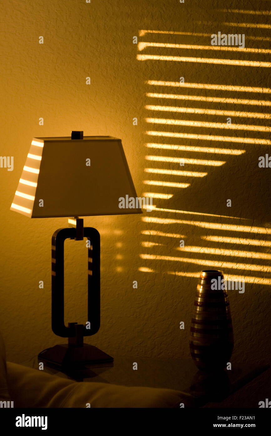 Strahlender Sonnenschein in einem dunklen Raum wirft Linien über Jalousien  bis hin zu einer Lampe Stockfotografie - Alamy