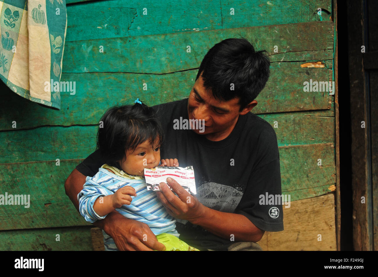 Guatemala, San Cristobal, Kind am Knie des Vaters sitzen und Essen plumpy Nut (Adolfo Cal Lem 35 und Aracely Noemi Cal Cap 1 Jahr 3 Monate) Stockfoto