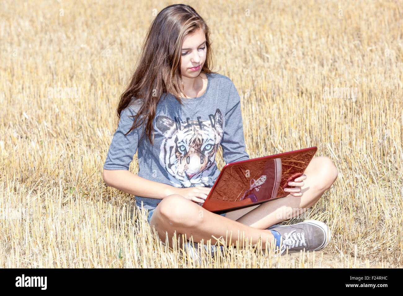 Junger Teenager mit Notebook, Teenager-Mädchen mit Laptop auf einem Stoppelfeld, Globale Kommunikation mit drahtloser Technologie, Lifestyle außerhalb des Konzepts Stockfoto