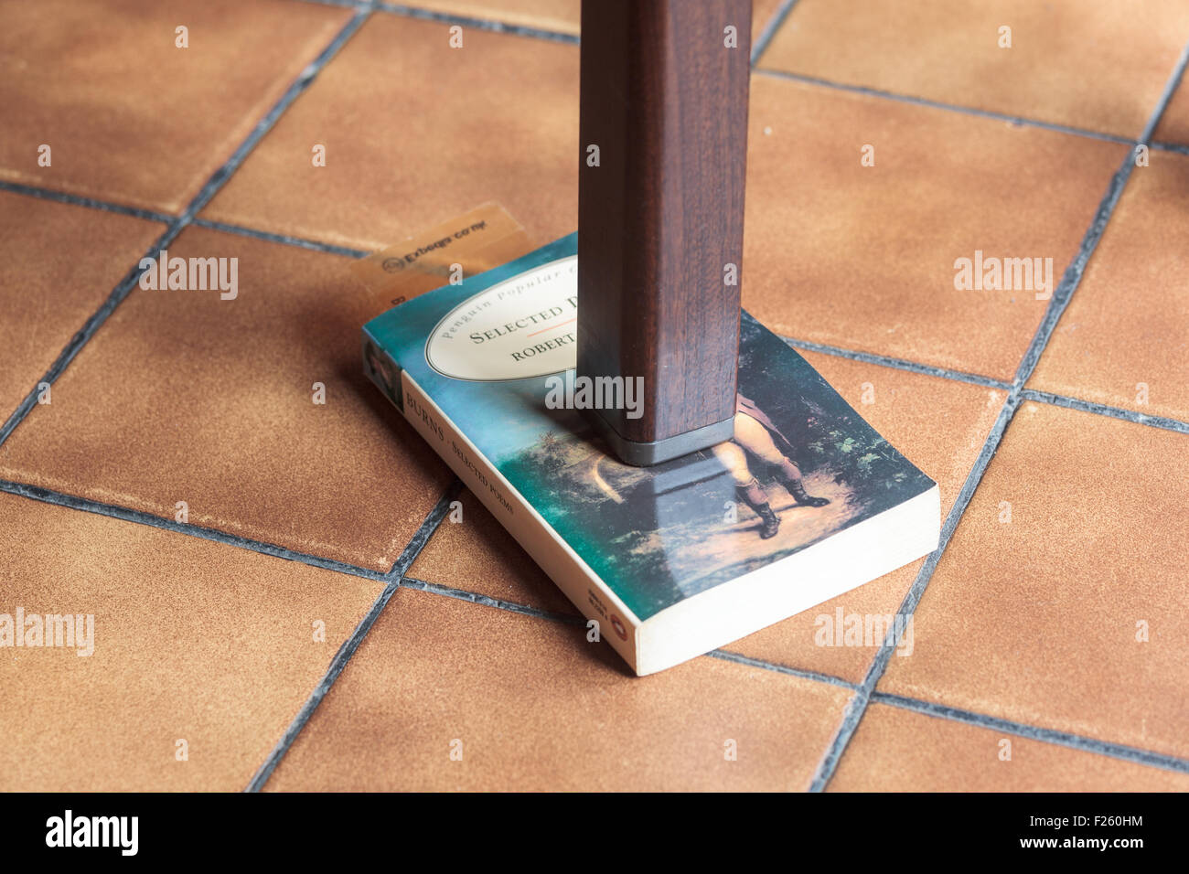 Bein einem wackligen Tisch, unterstützt durch ein Buch Stockfoto