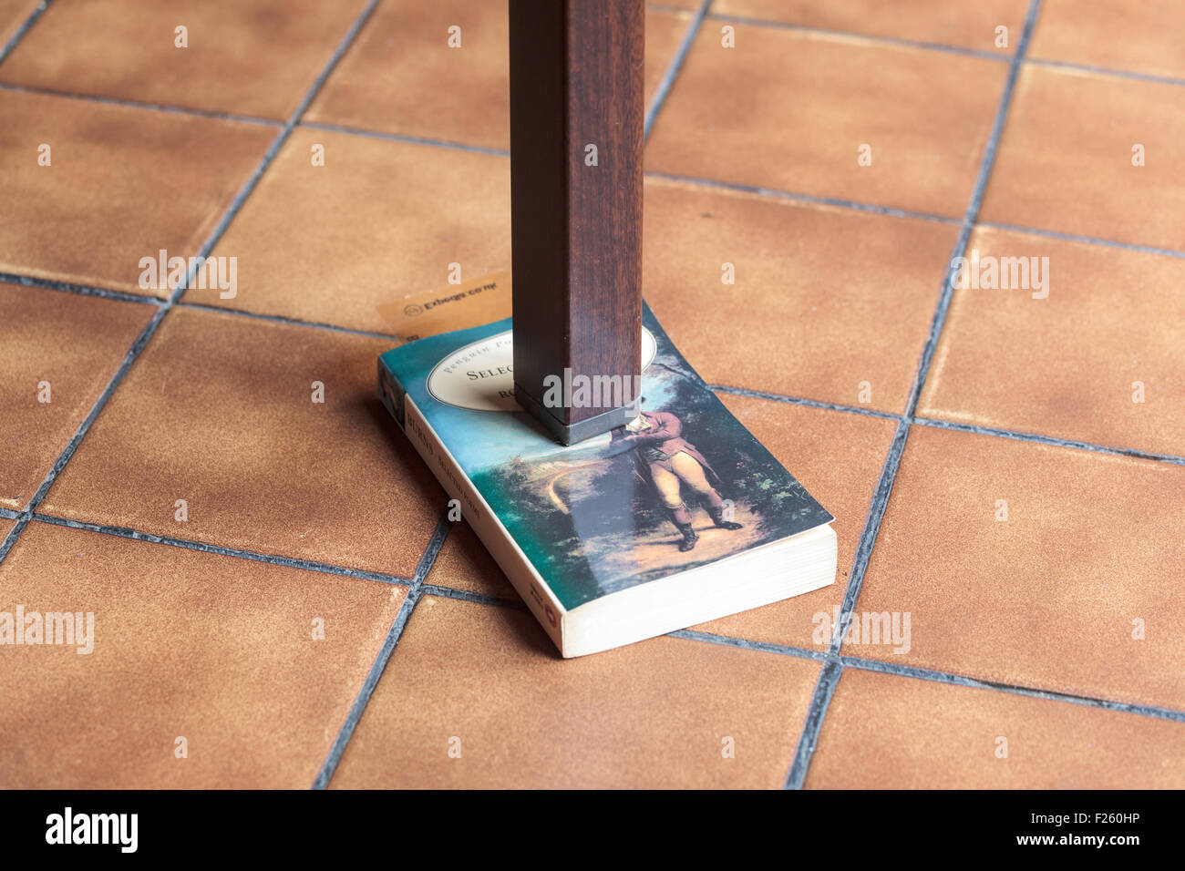 Bein einem wackligen Tisch, unterstützt durch ein Buch Stockfoto