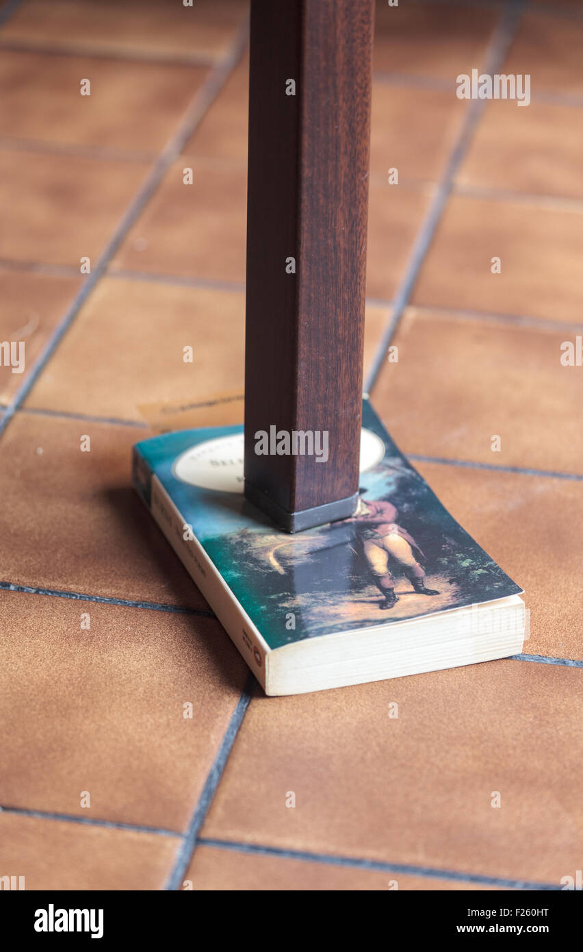 Bein einem wackligen Tisch, unterstützt durch ein Buch Stockfoto
