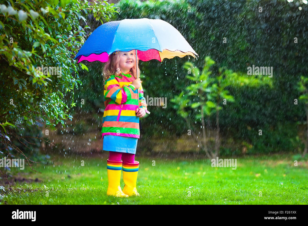 Kleines Mädchen mit bunten Regenschirm im Regen zu spielen. Kinder