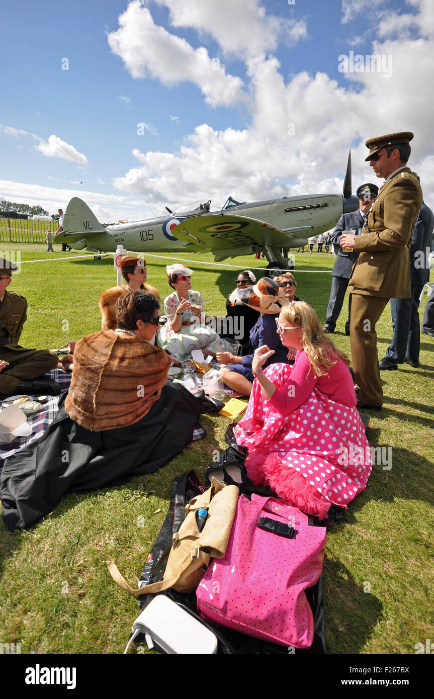 Goodwood Revival 2015. Picknick. Männer und Frauen im Zeitraum Kleidung genießen Sie ein Picknick auf dem Rasen mit dem Zweiten Weltkrieg Ebene Stockfoto