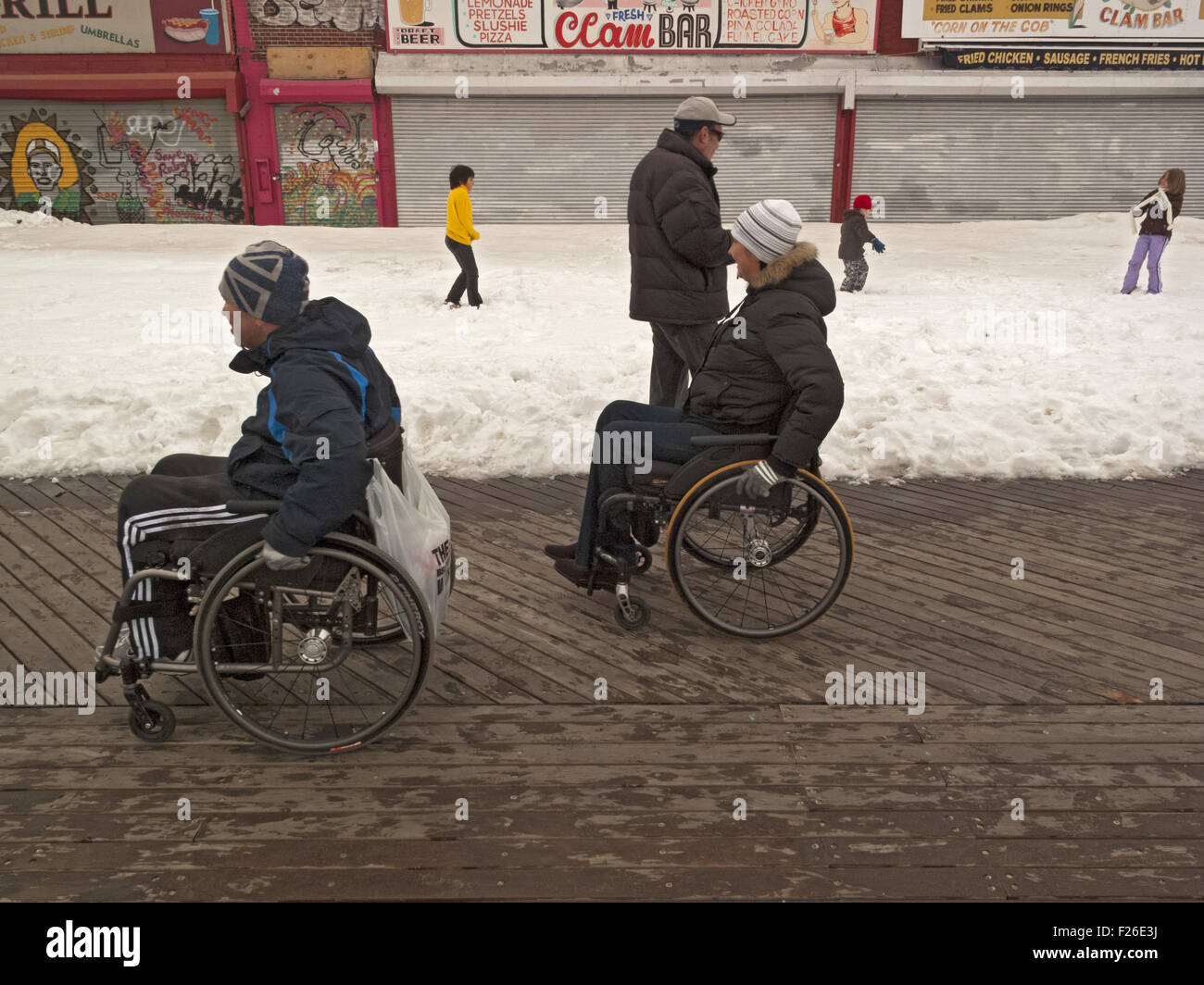 Paar navigieren Coney Island Boardwalk im Rollstuhl, wie Kinder im Schnee in Brooklyn, New York, 2011 spielen. Stockfoto