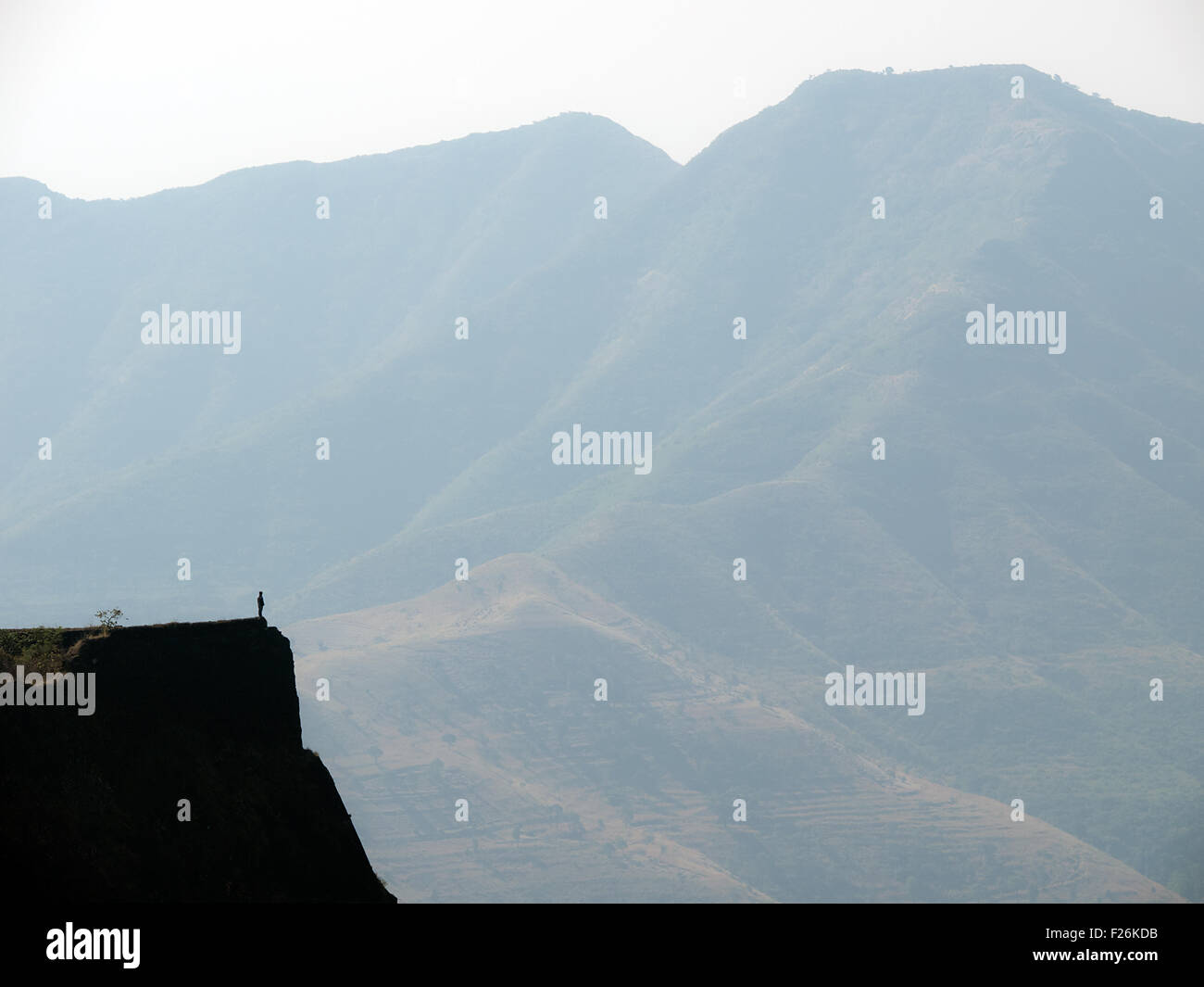Ein Mann steht am Rand einer Klippe gegen einen anderen großen Berg Stockfoto