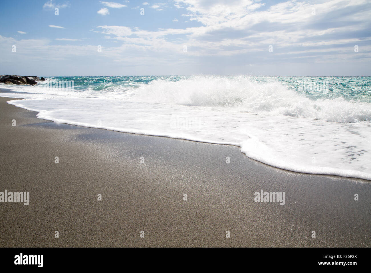 die Wellen brechen sich am einsamen Strand, der Hintergrund blauer Himmel und Wolken Stockfoto