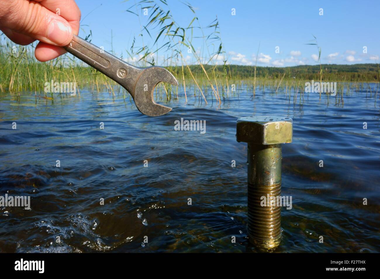 Umweltschutz: Finger mit einem Werkzeug vor einer großen Mutter in einem See. Stockfoto