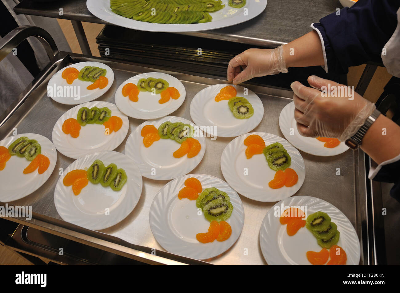 Ein Caterer bereitet Platten von Dessert mit Scheiben von Kiwi und Orange. Stockfoto