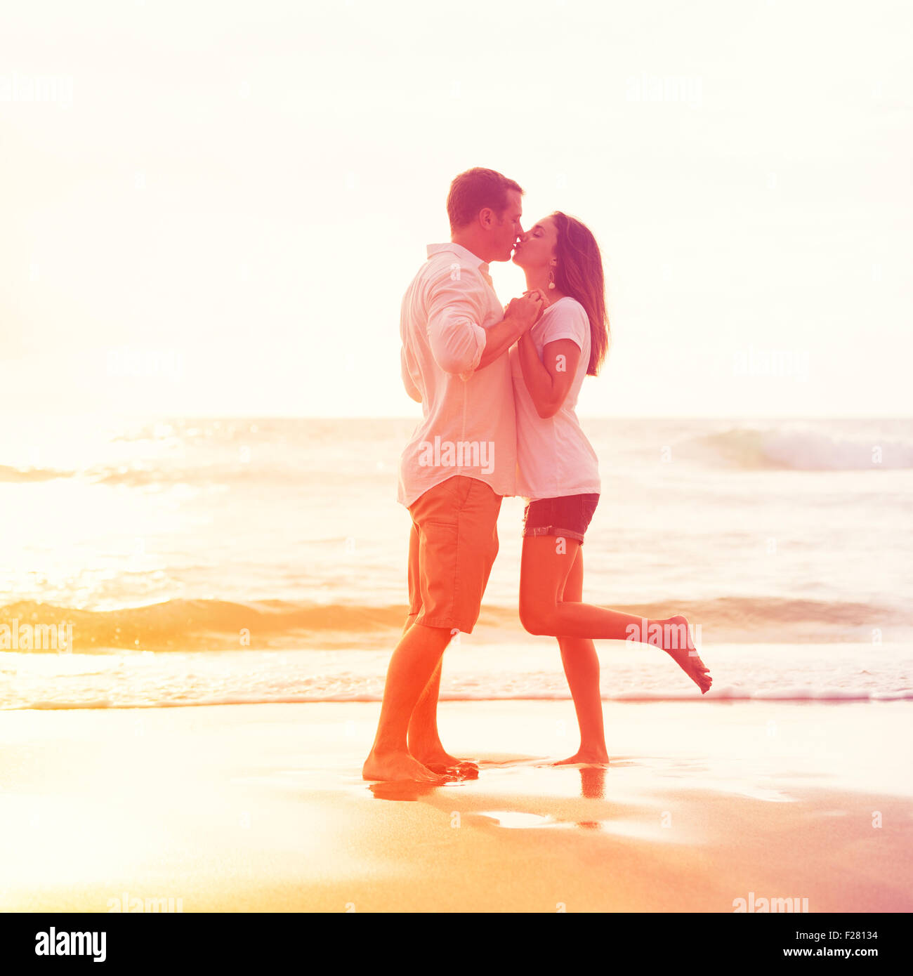 Romantisches Brautpaar küssen am Strand bei Sonnenuntergang Stockfoto