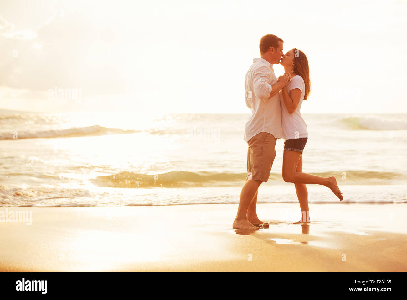 Romantisches Brautpaar küssen am Strand bei Sonnenuntergang Stockfoto