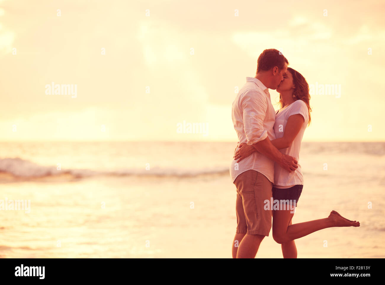 Romantisches Brautpaar küssen am Strand bei Sonnenuntergang Stockfoto