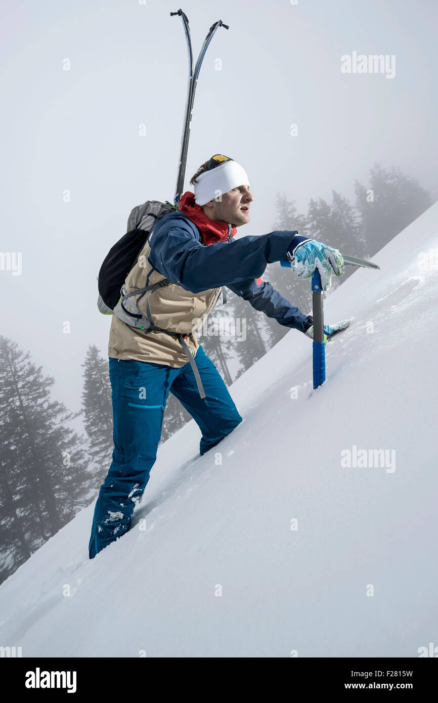 Männliche Bergsteiger hinauf verschneiten Hang mit Axt, Zell Am See, Österreich Stockfoto