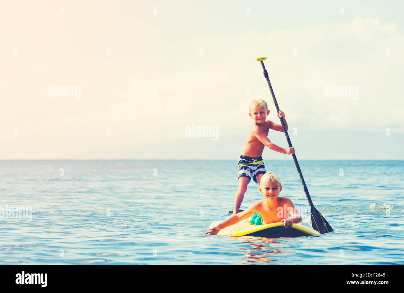 Jungen Spaß Stand Up Paddeln zusammen im Ozean Stockfoto