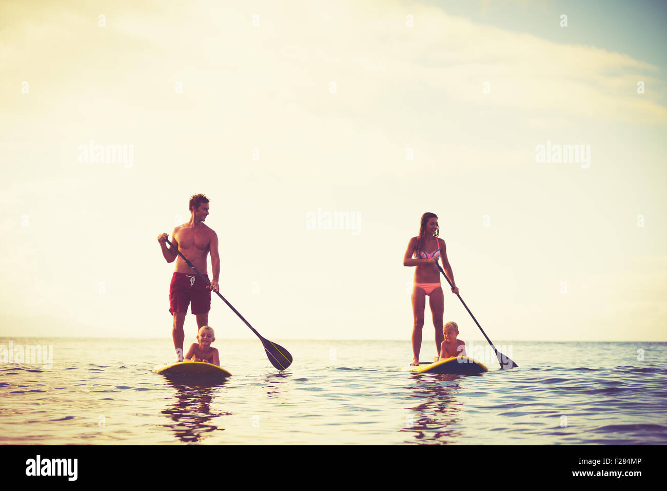Familie mit Spaß Stand Up Paddling zusammen im Meer bei Sonnenaufgang Stockfoto