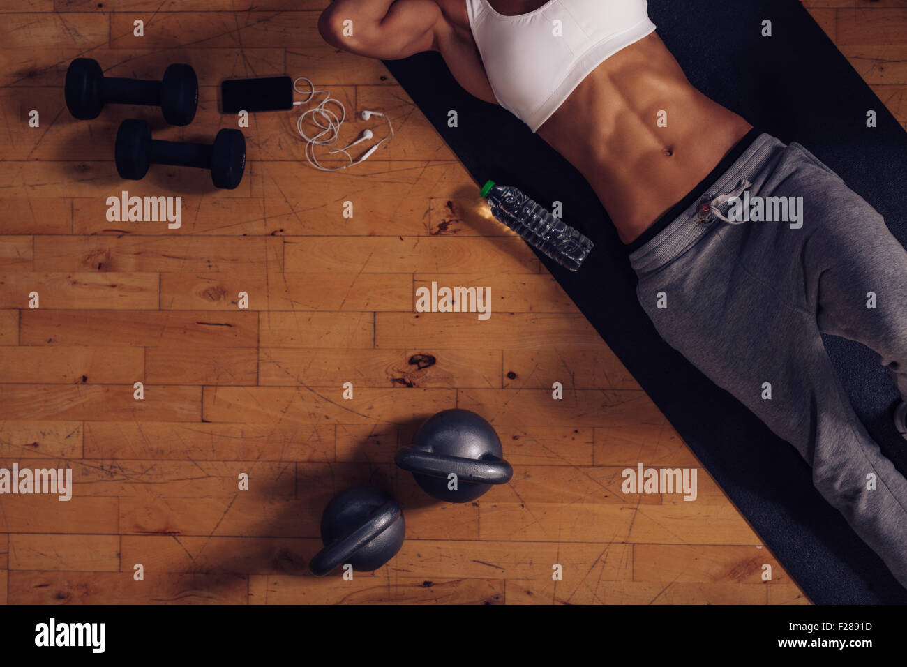 Draufsicht der jungen Frau liegt auf Yoga-Matte im Fitness-Studio. Entspannen nach dem Training mit einer Wasserflasche Hanteln Fitness-Frau ein Stockfoto
