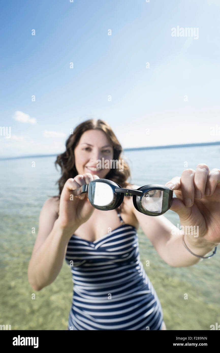 Reife Frau holding Schwimmbrillen und lächelnd am See, Bayern, Deutschland Stockfoto