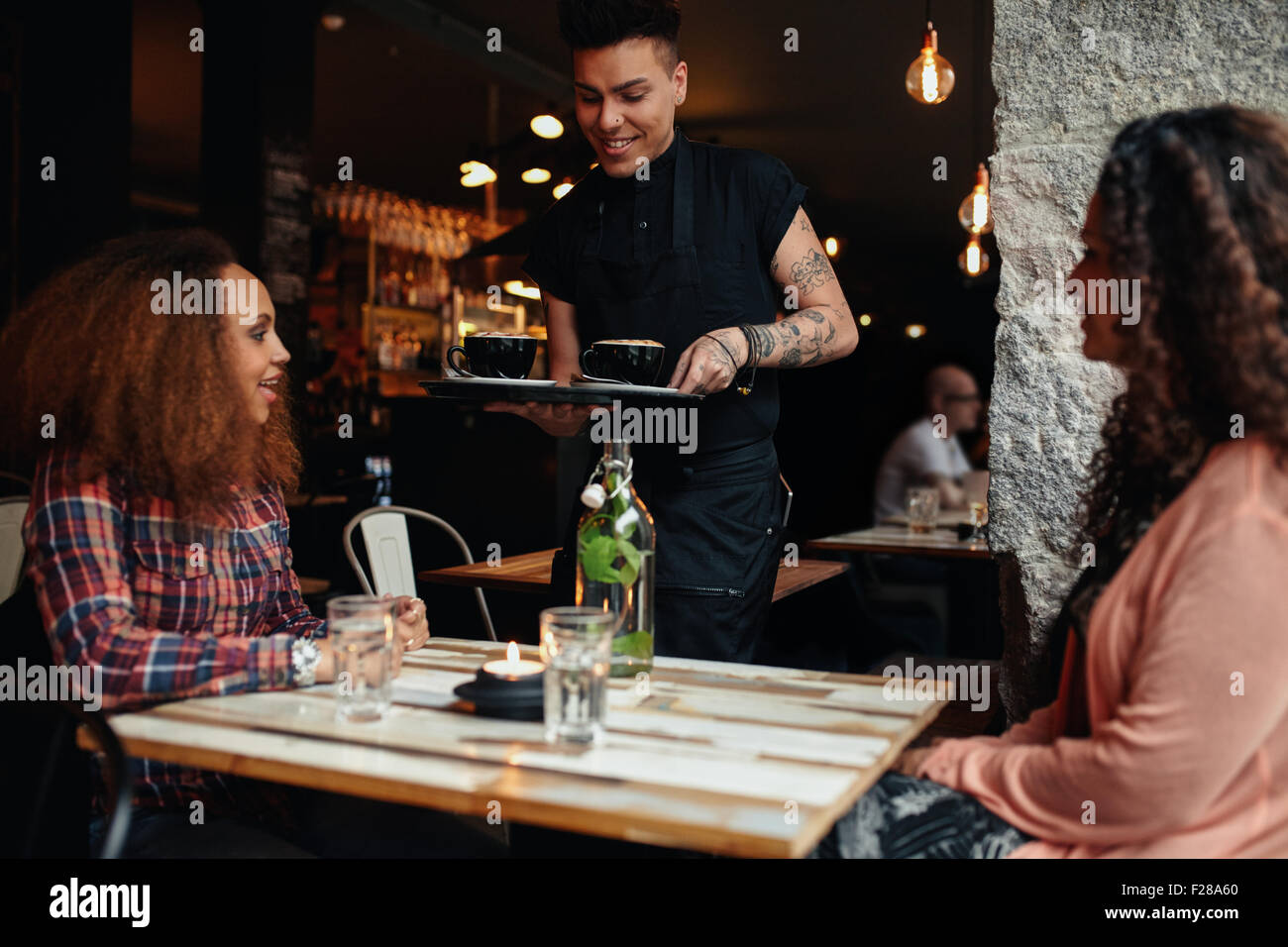 Zwei junge Frauen sitzen in einem Restaurant mit Kellner serviert Kaffee. Freundinnen im Coffee Shop. Stockfoto