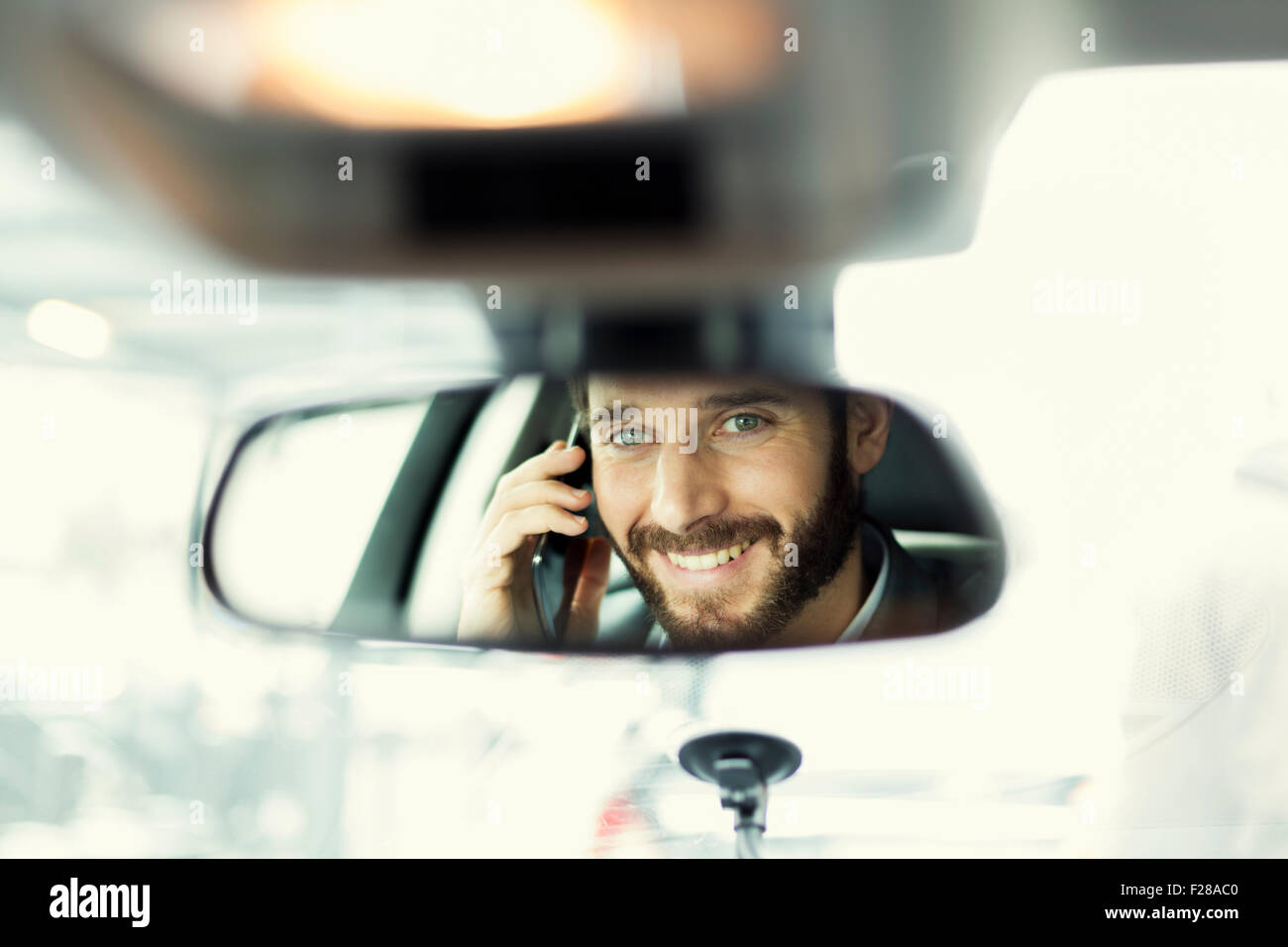 Fröhlicher Mensch auf Handy im Auto. Reflexion im Spiegel Stockfoto