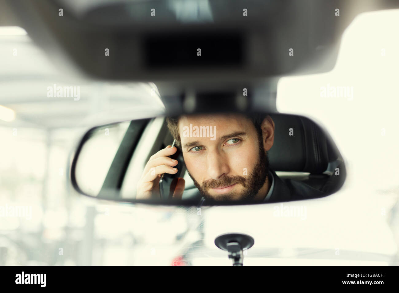 Fröhlicher Mensch auf Handy im Auto. Reflexion im Spiegel Stockfoto