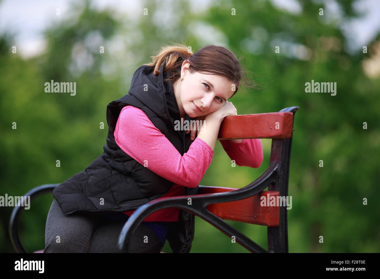 Hübsche junge Frau sitzt auf einer Parkbank. Ein Mädchen in einer entspannten Haltung ruht und in die Kamera schaut. Selektiven Fokus auf th Stockfoto