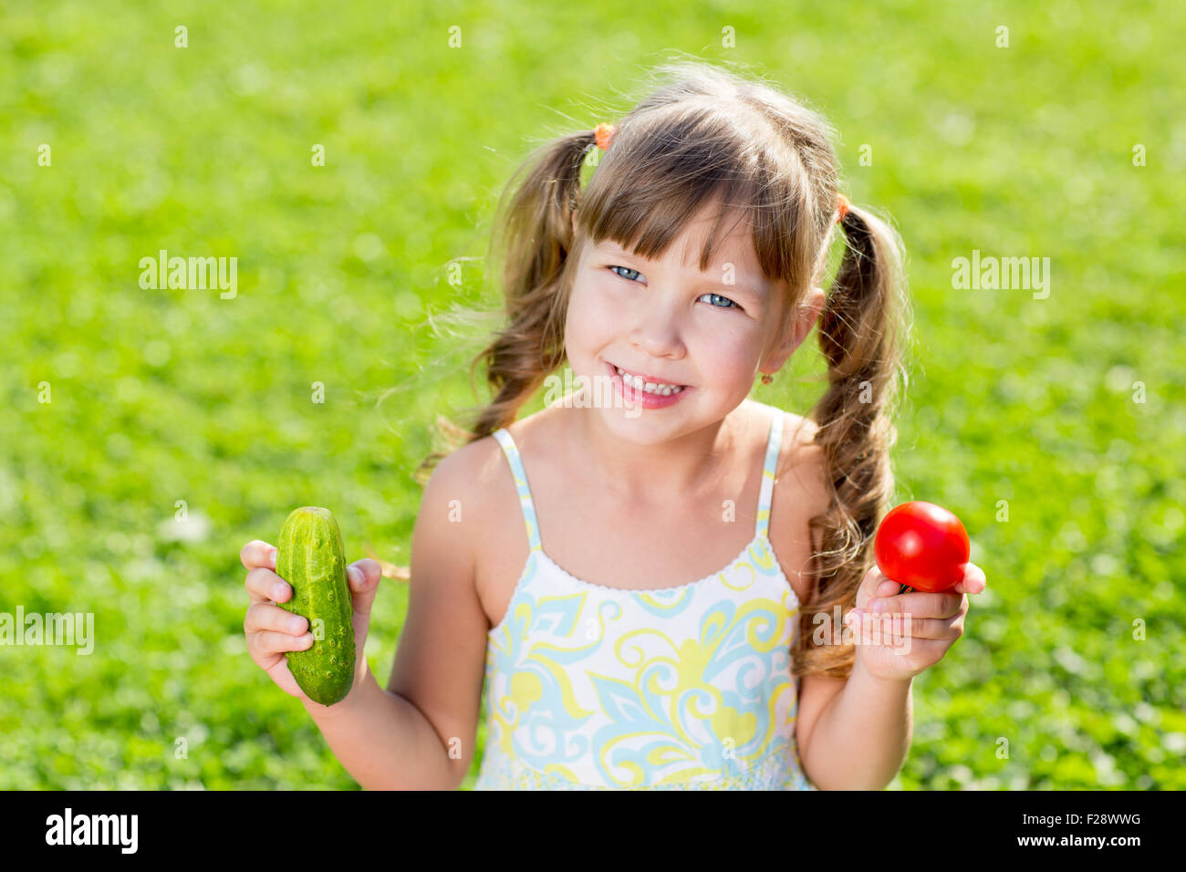 Glückliches Kind auf Sommer Rasen Hintergrund mit gesundes Gemüse in Händen. Stockfoto