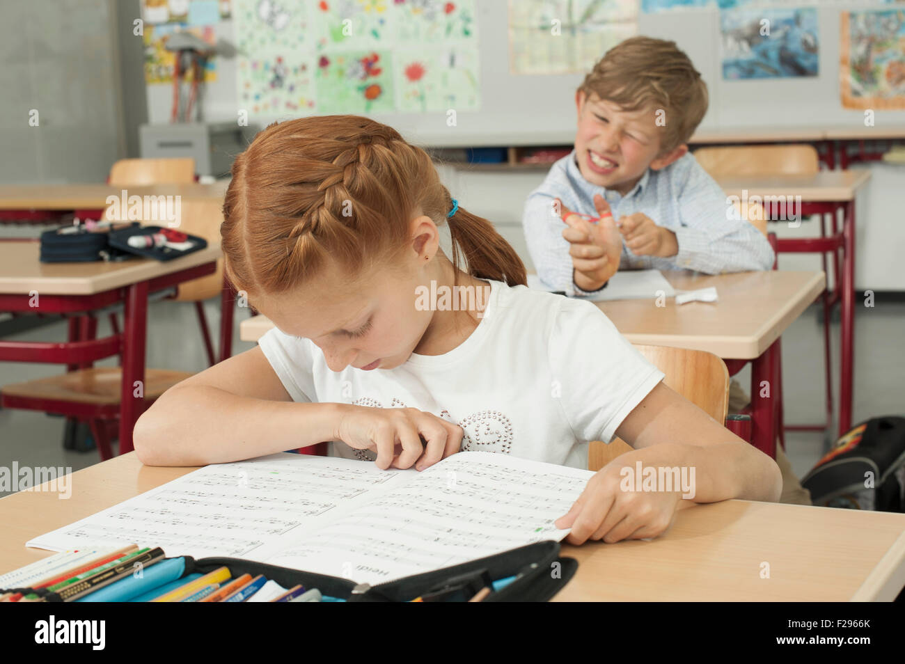 Schuljunge stört ein Schulmädchen mit Schleuder im Klassenzimmer, München, Bayern, Deutschland Stockfoto