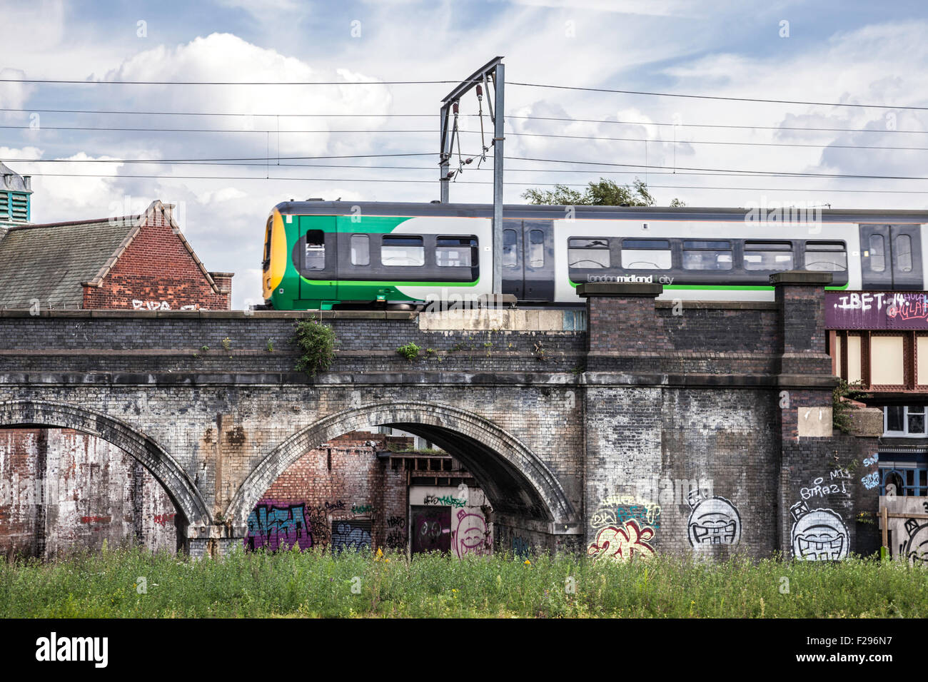 Ein London Midland-Zug überquert die Graffitied Bahn Bögen bei Selly Oak, Birmingham, England, UK Stockfoto