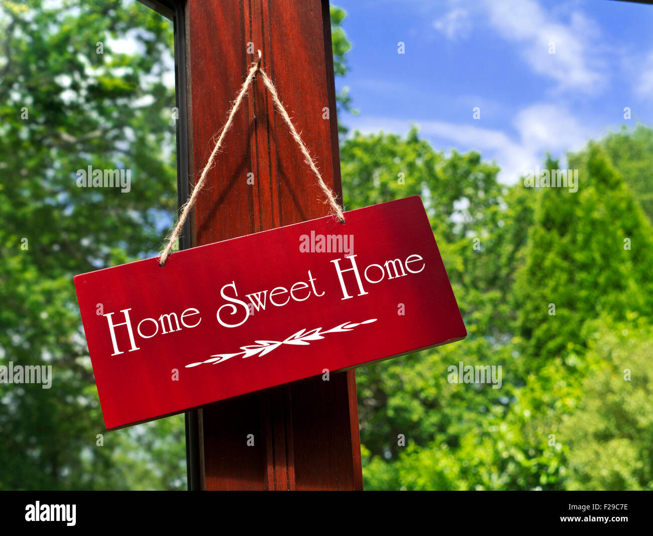 "Home Sweet Home" Holzschild hängen in einem Gartenzimmer mit Laub und blauer Himmel im Hintergrund Stockfoto