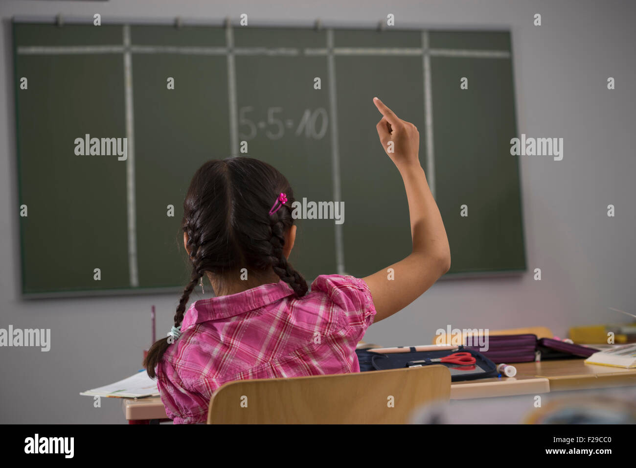 Schulmädchen vor der Tafel mit erhobener Hand im Klassenzimmer, München, Bayern, Deutschland Stockfoto