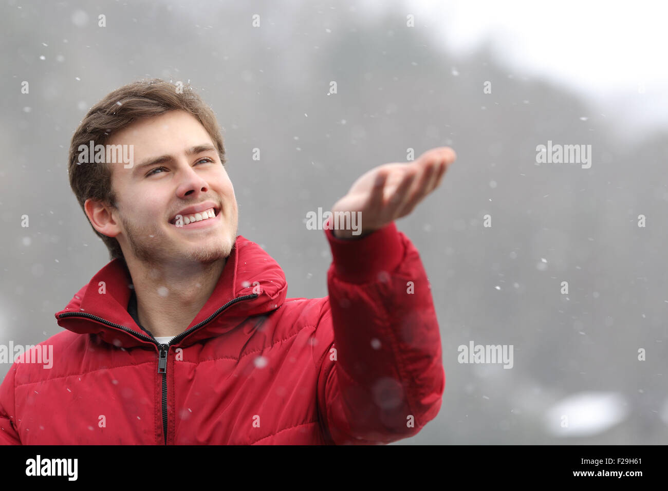 Glücklicher Mann mit einer roten Jacke gerade den Schnee, der auf seine Hand im winter Stockfoto