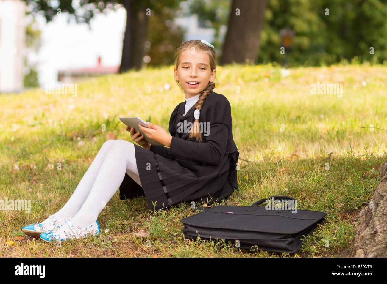 Kleine Studentin auf dem Rasen sitzen und mit Tablet-PC. Lächelnd Schüler Rest nach der Schule im Park im Freien. Stockfoto