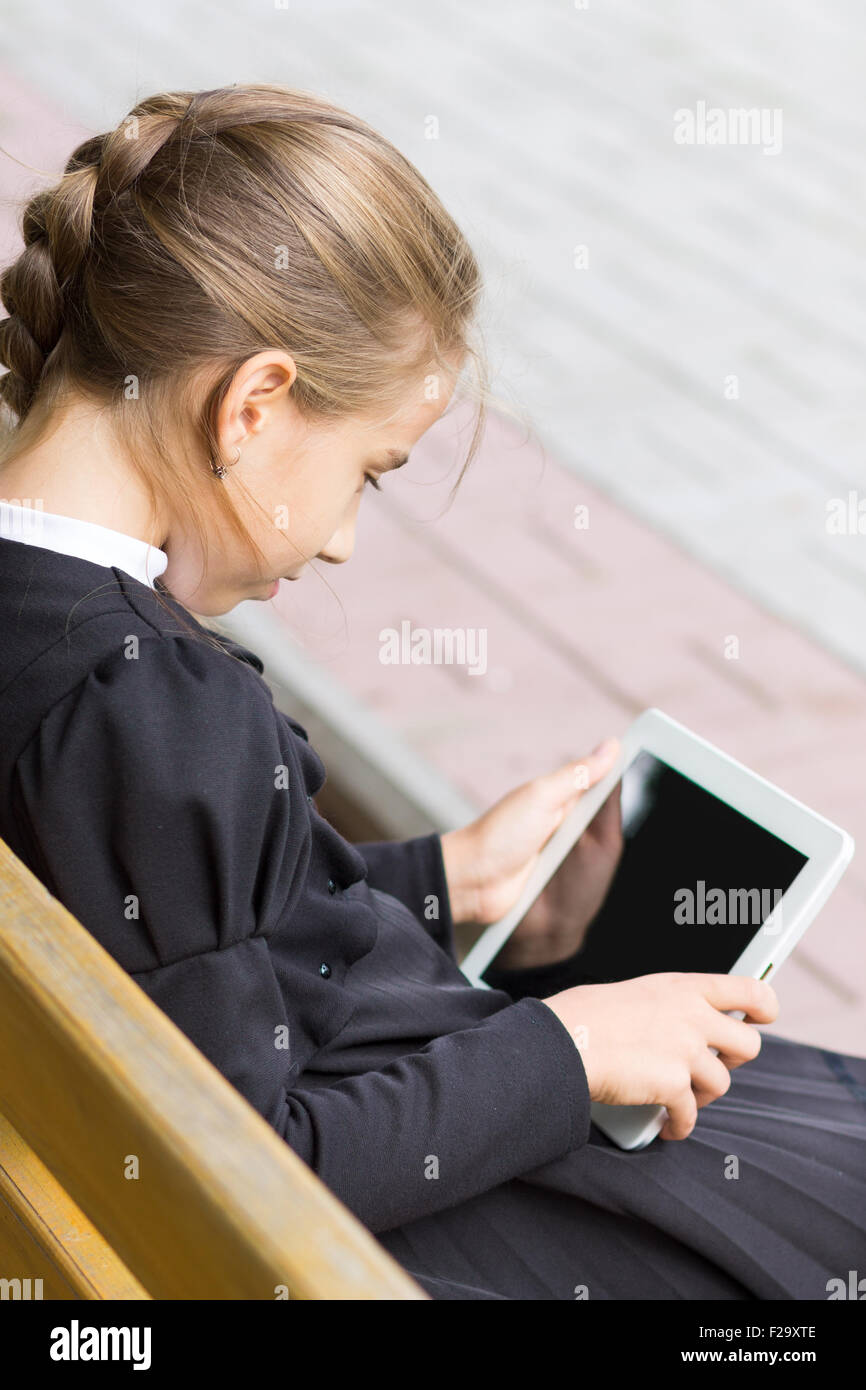 Kleine Schüler Mädchen mit Tablet auf der Bank sitzen. Schulmädchen spielt mit digitalen gadget Stockfoto