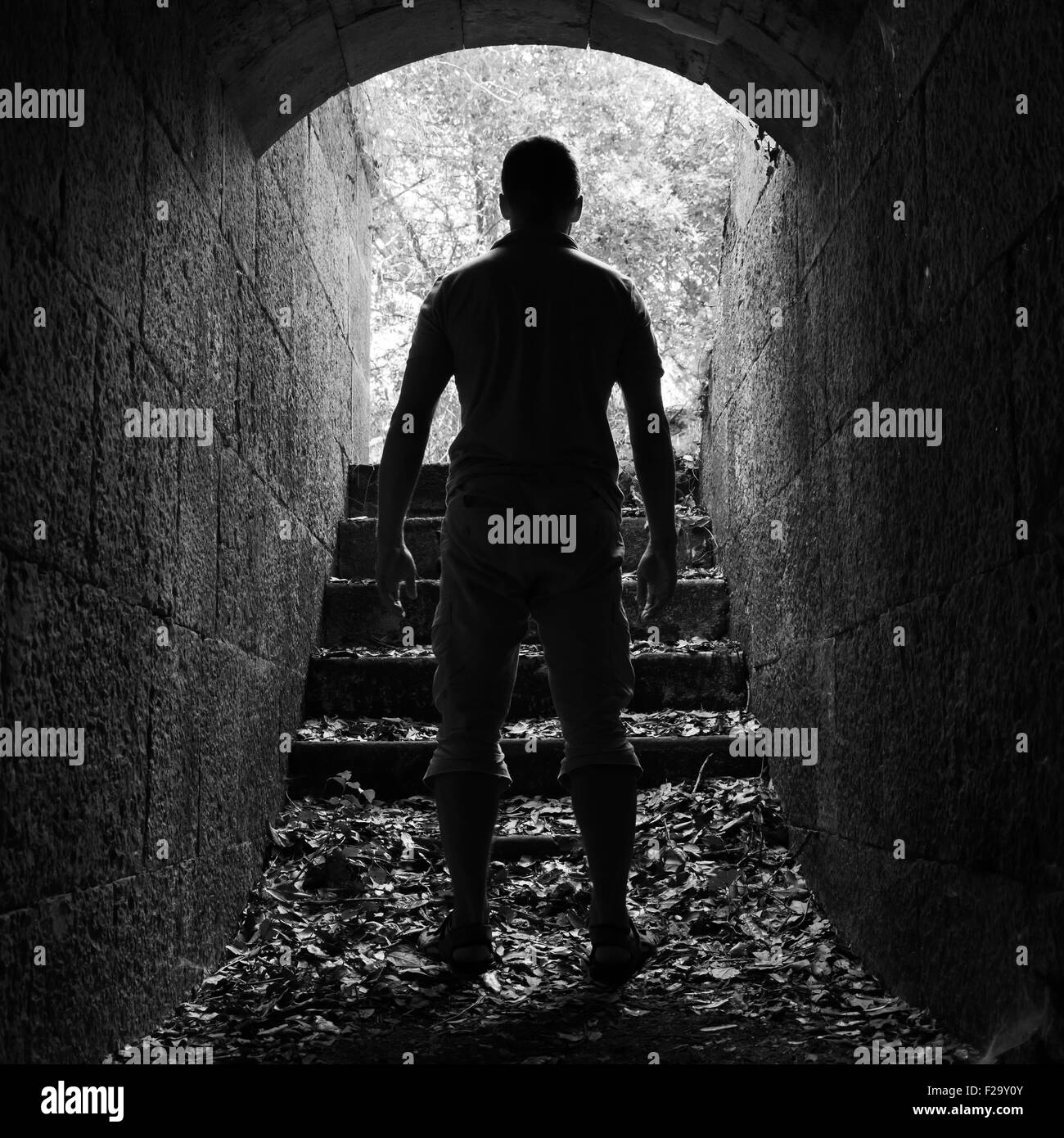 Junger Mann steht im dunklen Stein-Tunnel mit glühenden Ende, schwarze und weiße quadratische Foto Stockfoto