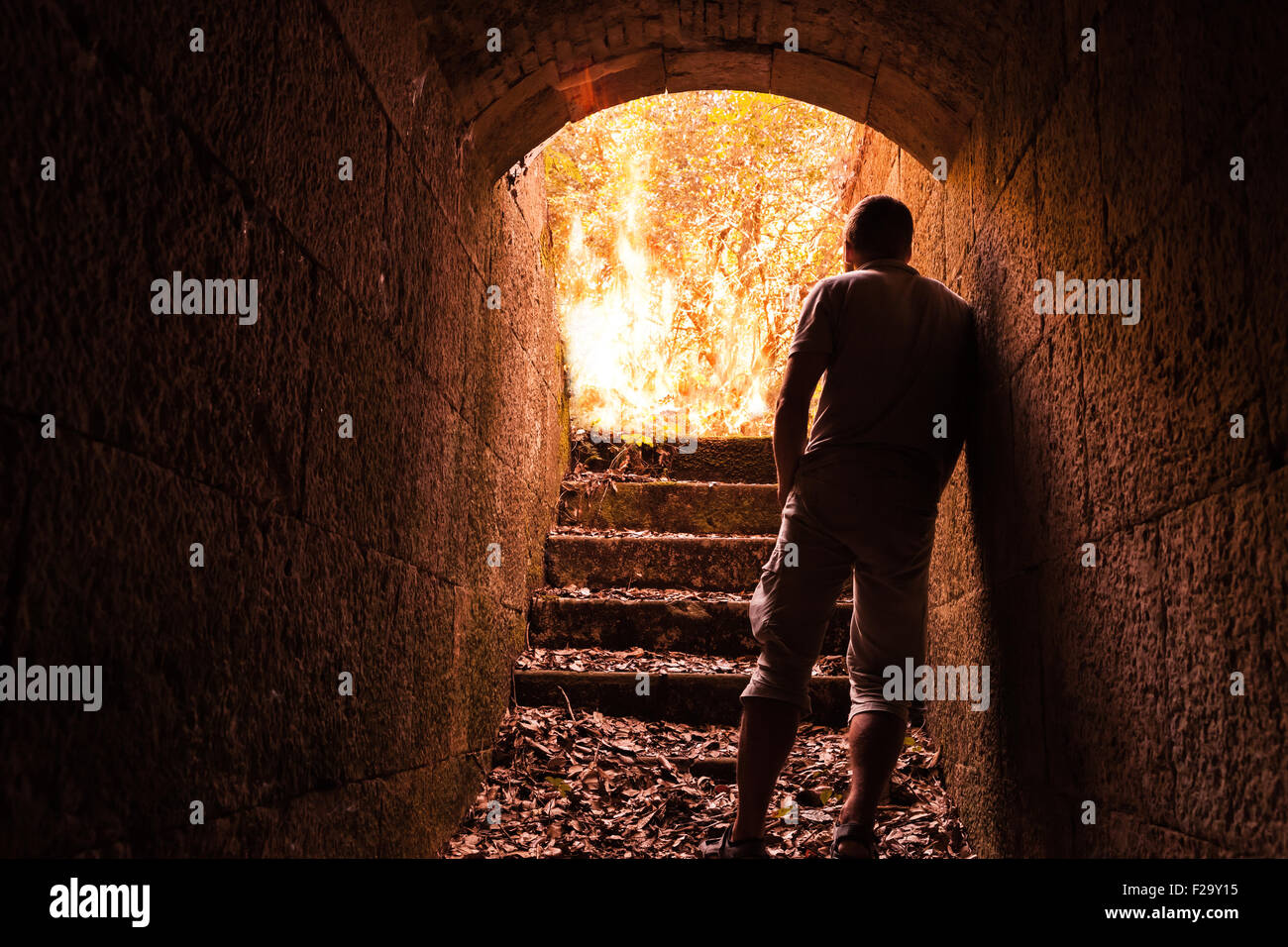 Junger Mann steht im dunklen Stein-Tunnel mit dem großen Feuer am Ende Stockfoto