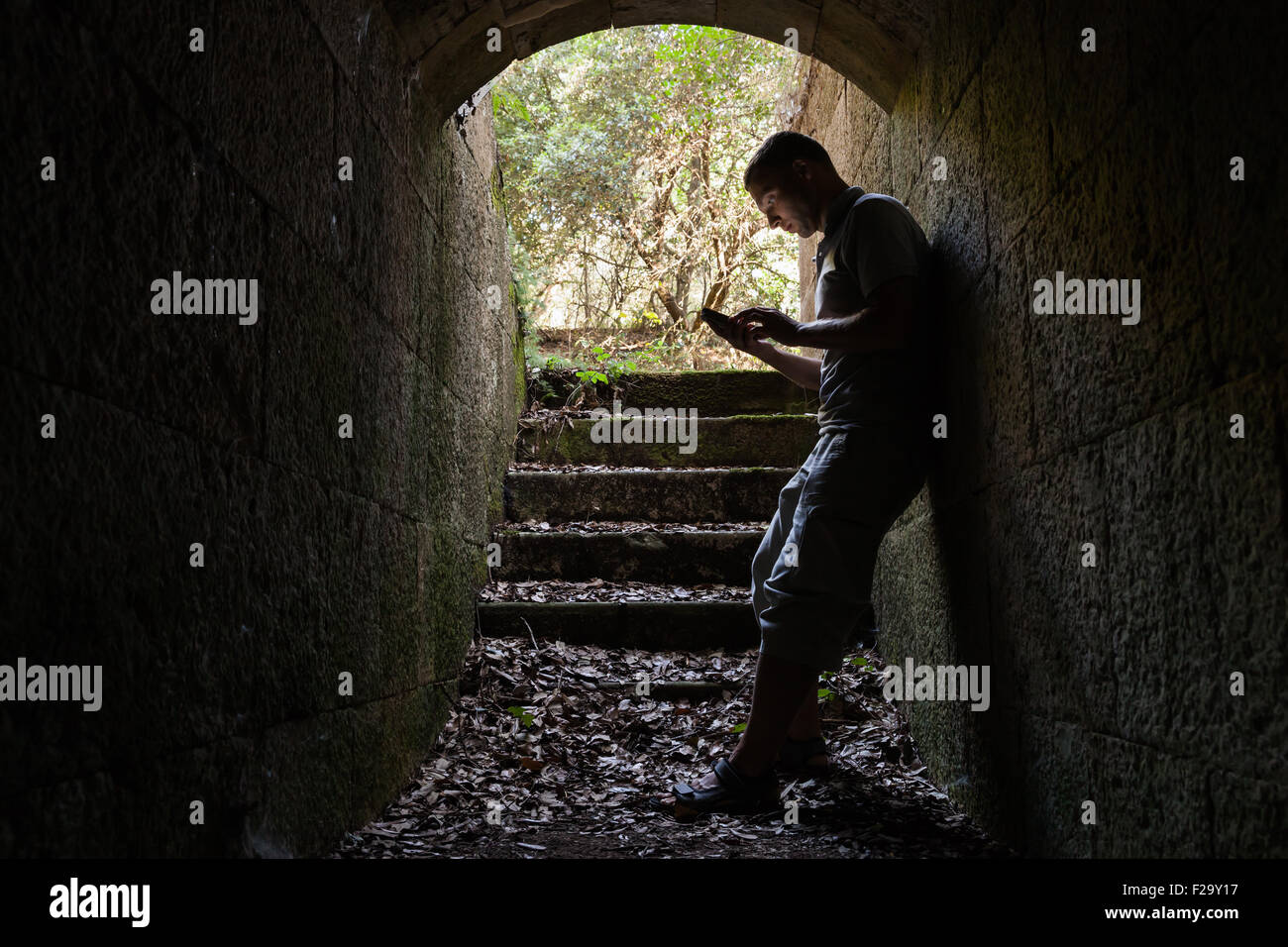 Junger Mann arbeitet auf ein Smart-Phone im dunklen Stein-tunnel Stockfoto