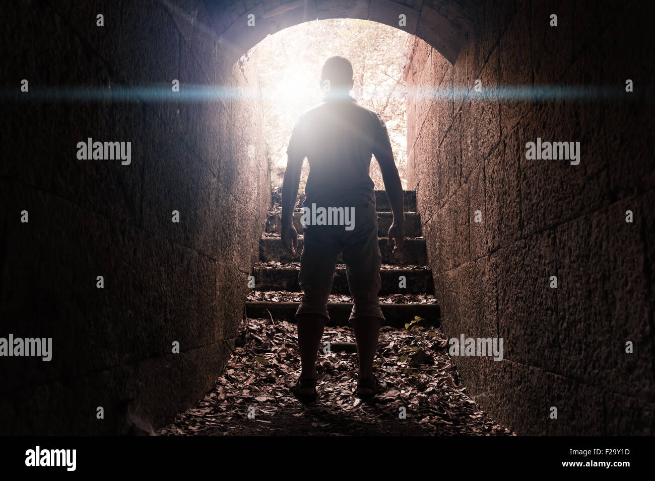 Junger Mann steht in dunklen Stein Tunnel mit glühenden Ende, warm getönten Foto mit Linse glow Effekt Stockfoto