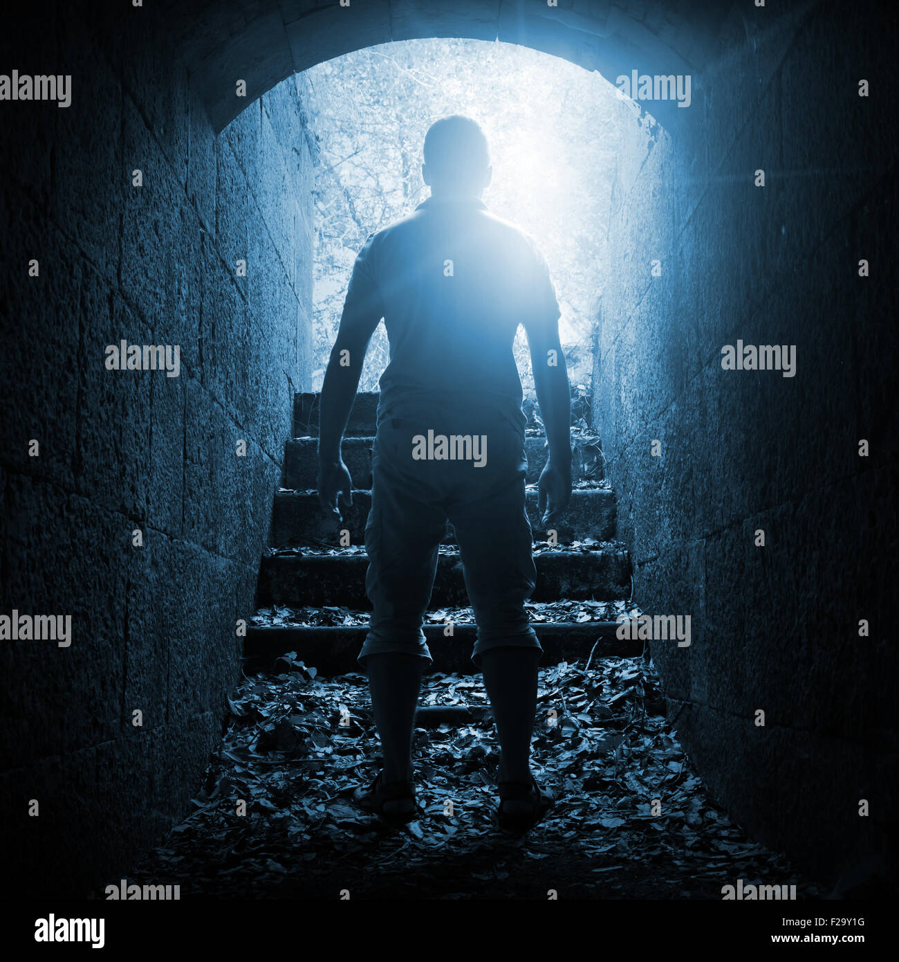 Junger Mann steht im dunklen Stein-Tunnel mit glühenden Ende, blau getönten quadratischen Foto Stockfoto