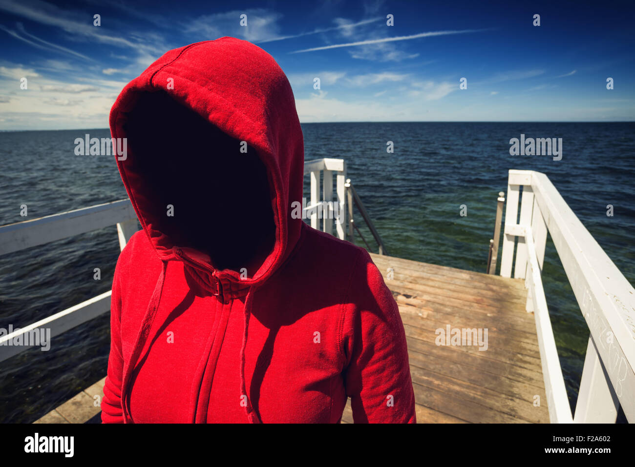 Entführung-Konzept, gesichtslosen Kapuzen unkenntlich Frau am Ozean Pier, unbekannte unheimlich weiblich im roten Hemd Stockfoto
