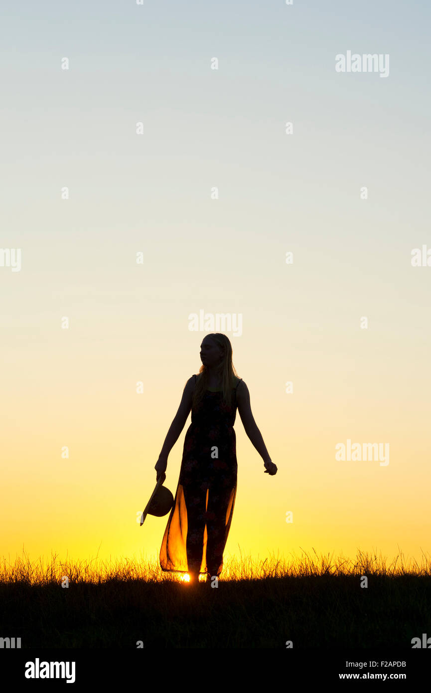 Teenager-Mädchen stand halten einen Hut bei Sonnenuntergang. Silhouette Stockfoto