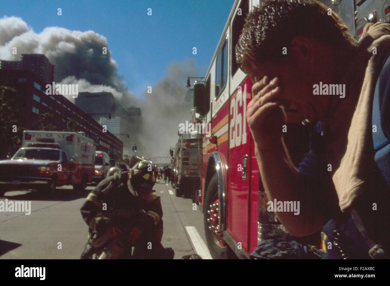 New York City Feuerwehrmann nördlich der eingestürzten Zwillingstürme. Hinter ihm sind andere Feuerwehrleute, Feuerwehrautos und Rettungsfahrzeugen. Im Hintergrund ist Rauch und pulverisierte Bauschutt der eingestürzten Nord- und Süd-Türme des World Trade Centers. New York City, 11. September 2001. (BSLOC 2015 2 41) Stockfoto