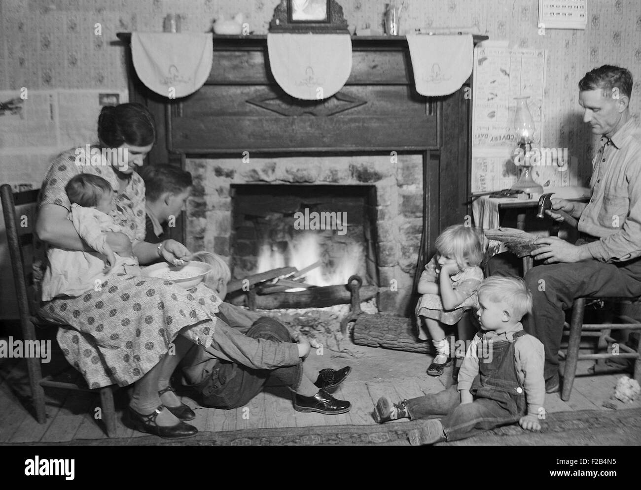 Carden Fletcher ist ein Nachtwächter Bunkhouses am TVA Norris-Staudamm. Einen Schuh repariert er beim Sitzen am Kamin mit seiner Frau und Familie, einschließlich 5 seiner 12 Kinder. November 1933 in Andersonville, TN Foto von Lewis Hine. -(BSLOC 2015 1 179) Stockfoto
