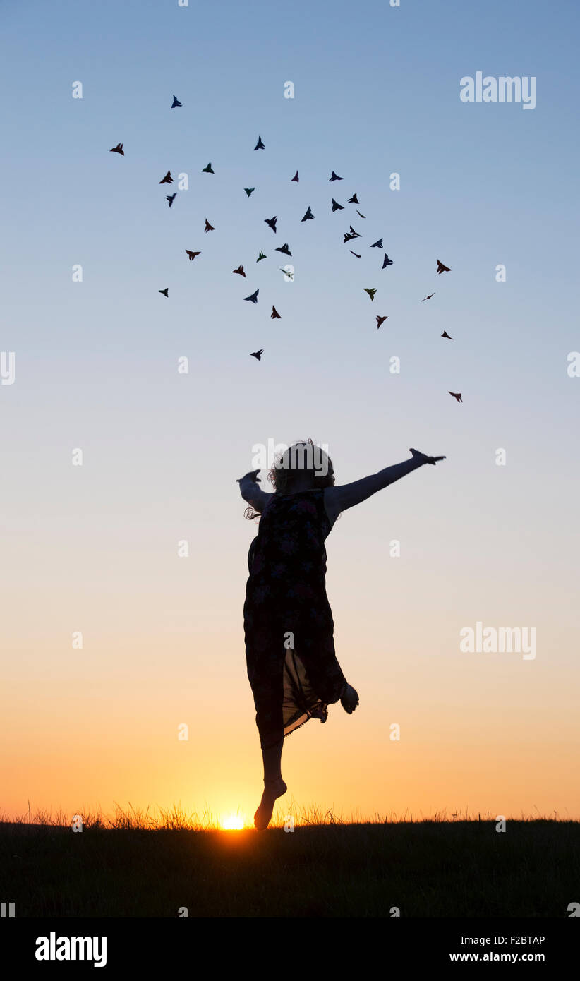 Teenager-Mädchen werfen Origami Schmetterlinge in der Luft bei Sonnenuntergang. Silhouette Stockfoto