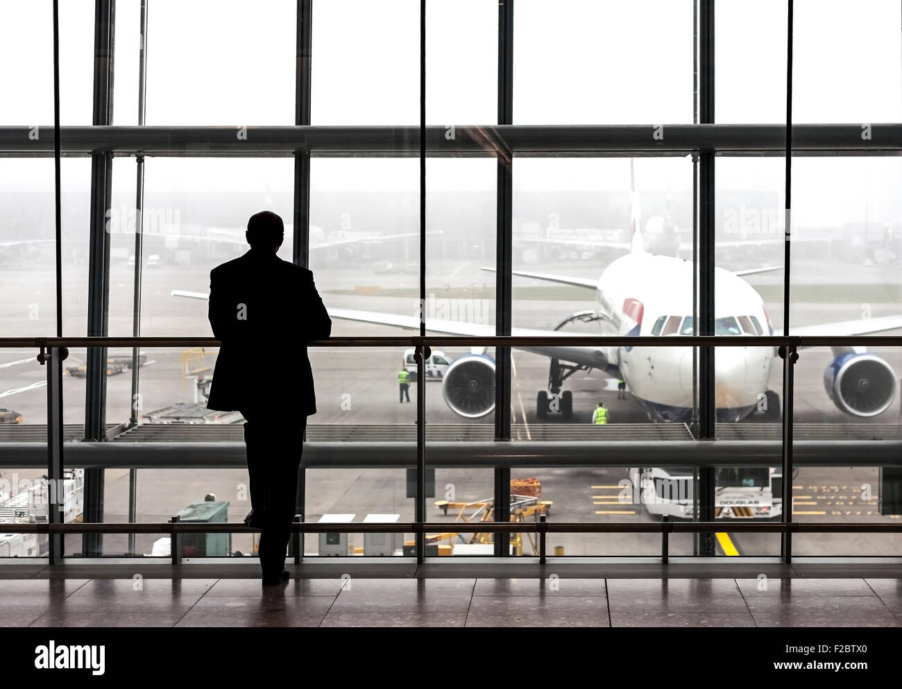 London, UK - 14. August 2015: Silhouette eines Reisenden warten auf ein Flugzeug in der Abflughalle Heathrow Flughafen an einem regnerischen Tag Stockfoto