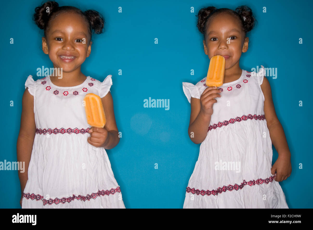 zwei eineiige Zwillingsmädchen Essen Popscicles auf blauem Hintergrund Stockfoto