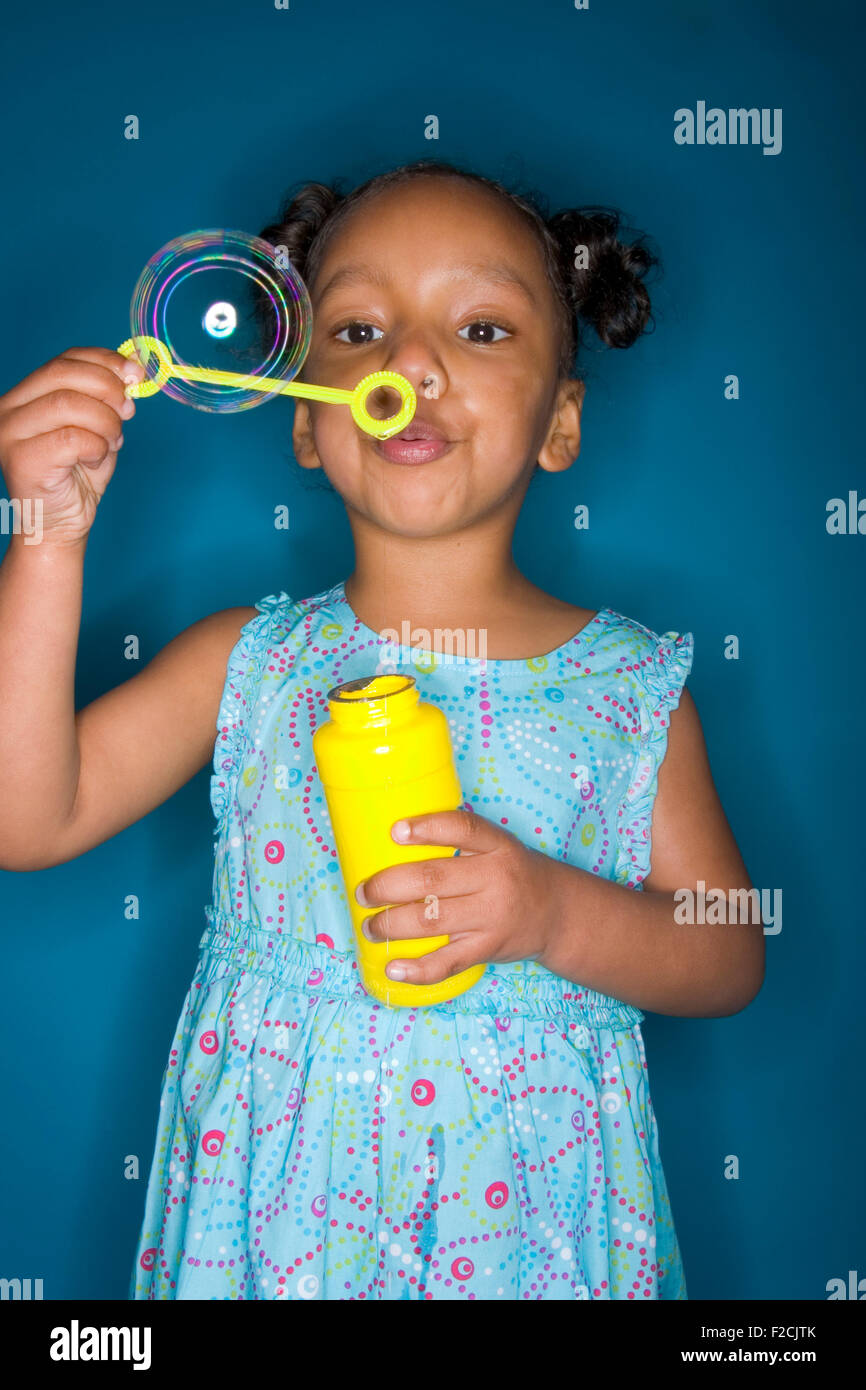 junge schwarze Mädchen in blau Sonnenkleid bläst Luftblasen in Studioumgebung mit blauem Hintergrund Stockfoto