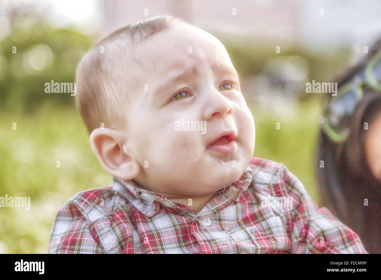 Das unschuldige Glück eine süße 6 Monate alte Babys mit hellbraunen Haaren in Rot kariertes Hemd und Beige Hose lächelnd in einem Stadtpark Stockfoto