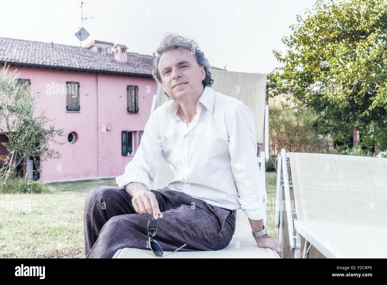faszinierende wohlhabenden Gentleman von vierzig aus Stadt ruht auf einem Liegestuhl im Garten von einem roten Landhaus in Italien Stockfoto