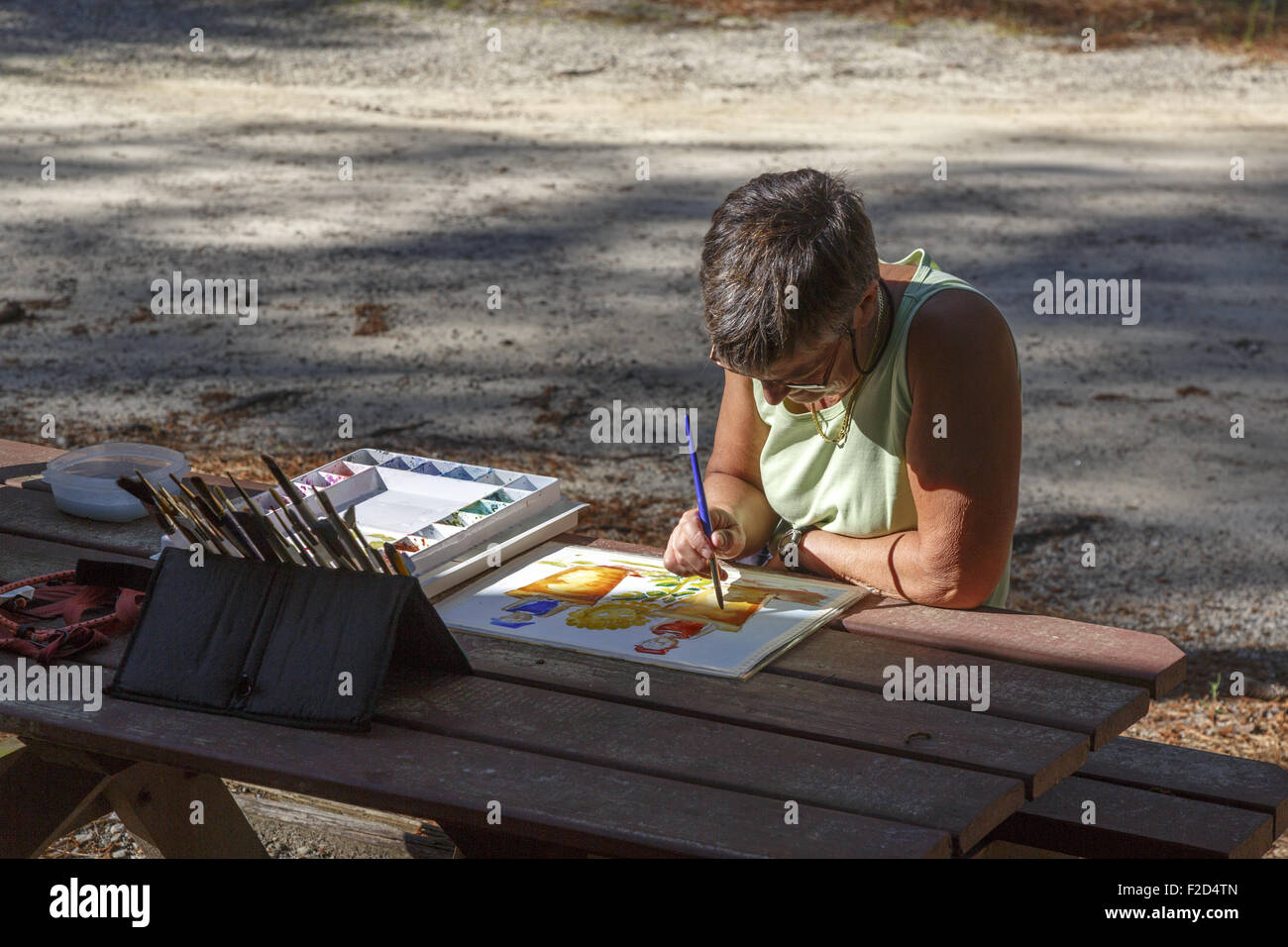 Künstlerin am Tisch sitzen in seitlichem Sonnenlicht Malerei Stockfoto